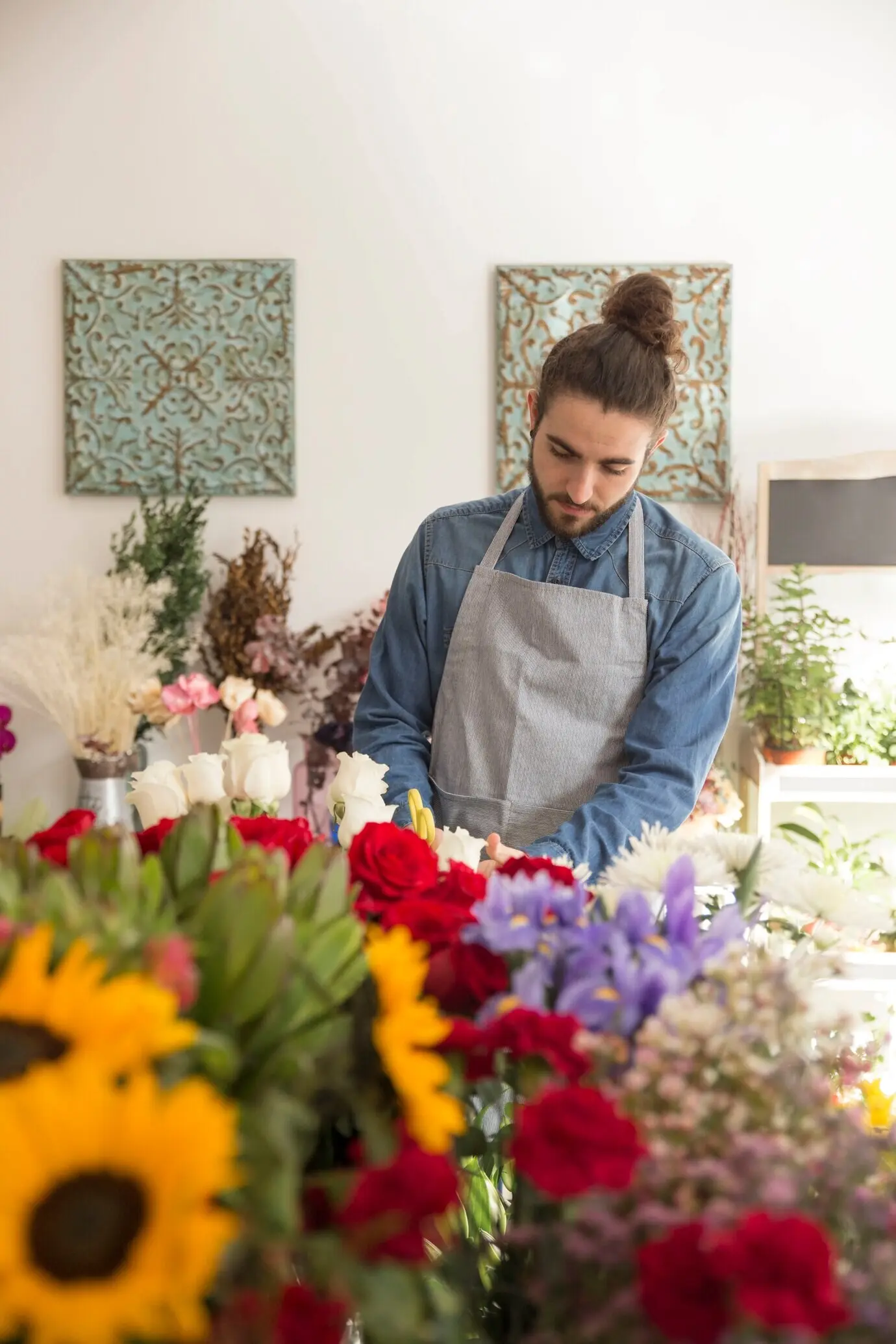 Porträt eines jungen männlichen Floristen in Schürze, der sich um schöne Blumen kümmert.